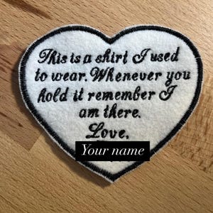 May include: White heart-shaped fabric patch with black embroidered text that reads: "This is a shirt I used to wear. Whenever you hold it remember I am there. Love, Your name".