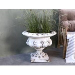 May include: A white pedestal planter with a wide, flared rim and a square base, featuring distressed dark grey detailing along the embossed floral and scalloped patterns. The urn-shaped vessel contains a cluster of tall, thin green ornamental grasses.