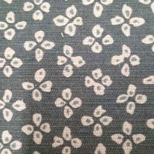 May include: Close-up of fabric featuring a repeating floral design. The background is a muted teal, with white flowers and a subtle teal centre. The fabric has a textured appearance.