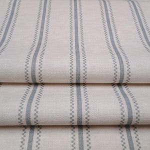 May include: Close-up of a folded fabric with a white background and thin, grey, vertical stripes. The fabric has a subtle texture.