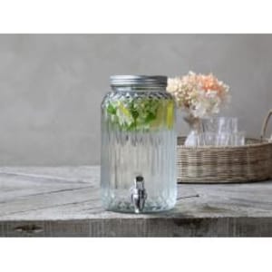 May include: A clear glass beverage dispenser with a vertical ribbed texture and a silver-toned metal spigot at the base. The container features a matching silver-toned screw-top lid and is filled with water containing slices of lemon and green herbs.
