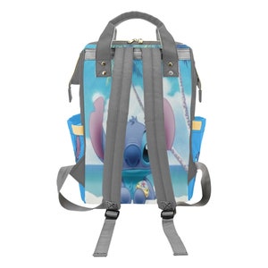May include: A gray backpack with adjustable straps. The backpack features a blue and white print of Stitch from Lilo & Stitch on a beach scene.