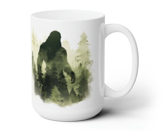 May include: White ceramic mug with a green silhouette of Bigfoot standing in a forest. The mug has a large handle.