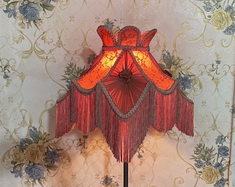 May include: A red lampshade with a fringe trim and a floral design. The lampshade is lit and casts a warm glow.