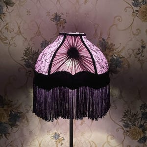 K&ouml;nnte beinhalten: Ein rosa und schwarzer Lampenschirm mit Fransenbesatz. Der Lampenschirm hat ein Blumenmuster und einen schwarzen Samtbesatz.