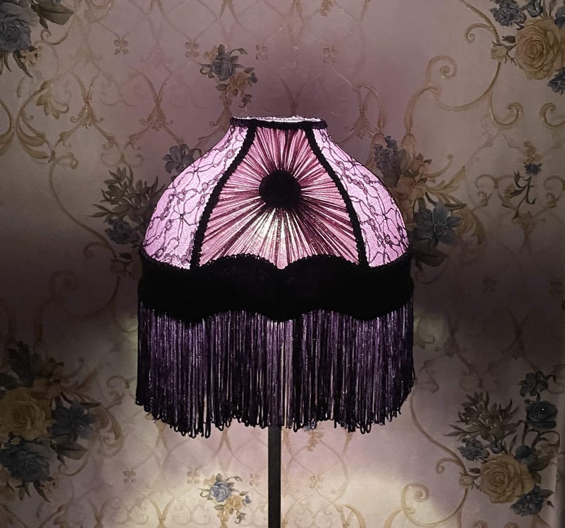 K&ouml;nnte beinhalten: Ein rosa und schwarzer Lampenschirm mit Fransenbesatz. Der Lampenschirm hat ein Blumenmuster und einen schwarzen Samtbesatz.