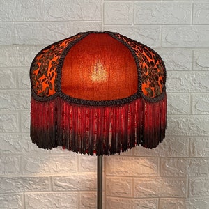 May include: A red and black lampshade with a beaded fringe. The lampshade has a floral pattern and is made of fabric.