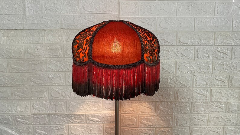 May include: A red and black lampshade with a beaded fringe. The lampshade has a floral pattern and is made of fabric.