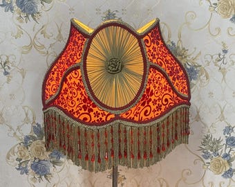 May include: A red and gold lampshade with a fringe trim. The lampshade has a floral pattern and a circular design in the center.