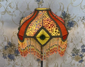 May include: A yellow, orange, and red lampshade with a beaded fringe. The lampshade has a geometric pattern and is made of fabric.