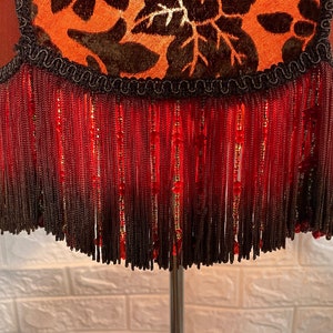 May include: A lampshade with a brown and orange floral pattern and a red fringe trim.