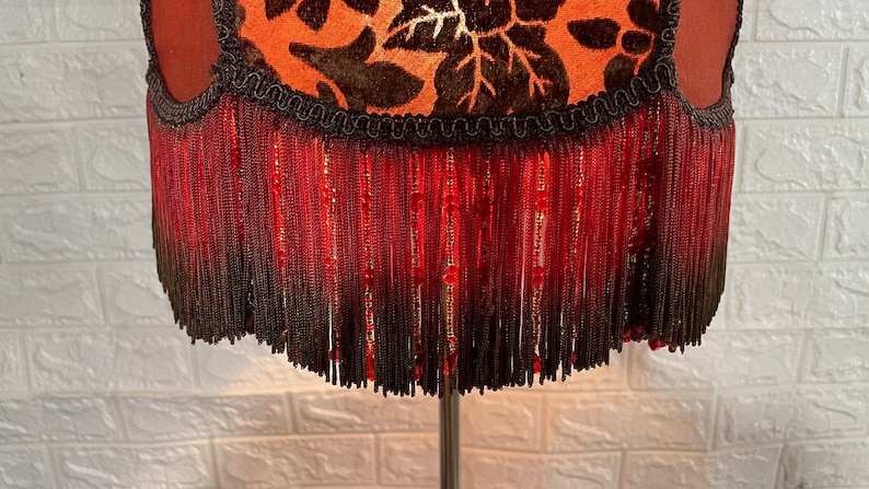 May include: A lampshade with a brown and orange floral pattern and a red fringe trim.