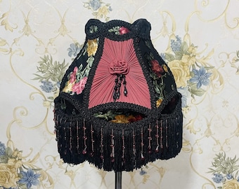 May include: A black and pink lampshade with floral embroidery and a beaded fringe. The lampshade has a pleated design and a floral pattern.
