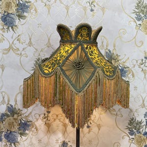 May include: A gold and green lampshade with a fringe trim. The lampshade has a geometric pattern and a floral design.