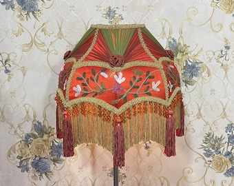 May include: A red and green lampshade with a floral design and gold trim. The lampshade has a fringe border and tassels.