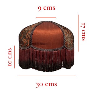 May include: A red lampshade with a gold and brown patterned fabric and a burgundy fringe trim. The lampshade measures 9 inches in diameter, 17 inches in height, and 30 inches in circumference.