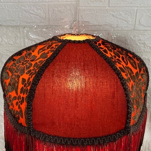 May include: A red lampshade with black and orange floral trim and a fringe bottom.