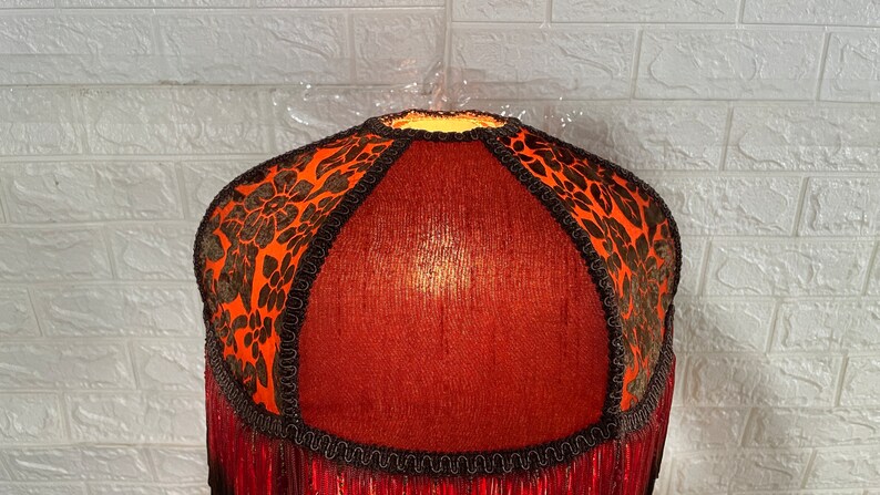 May include: A red lampshade with black and orange floral trim and a fringe bottom.