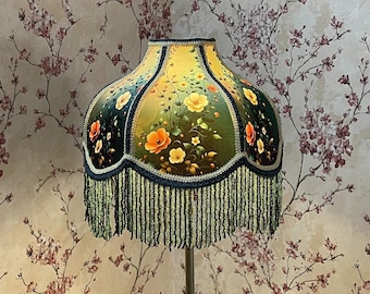 May include: A decorative lampshade with a floral design. The lampshade features a yellow and green background with orange and yellow flowers. The shade is trimmed with a dark blue border and green fringe.