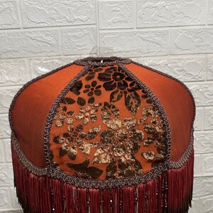 May include: A brown lampshade with a floral pattern and a fringe trim. The lampshade is made of fabric and has a round shape.