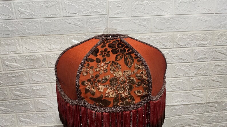 May include: A brown lampshade with a floral pattern and a fringe trim. The lampshade is made of fabric and has a round shape.
