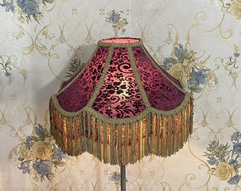 Puede incluir: Una pantalla de lámpara de terciopelo morado con flecos dorados y ribete de cuentas. La pantalla tiene un patrón floral y es de estilo vintage.