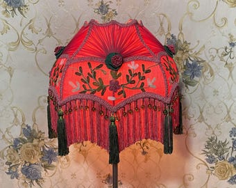 May include: A red lampshade with green embroidery and tassels. The lampshade is made of fabric and has a scalloped edge.