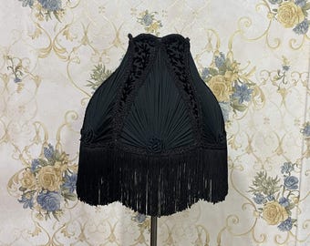 May include: A black lampshade with a pleated fabric design and a fringe trim. The lampshade is decorated with a floral pattern.
