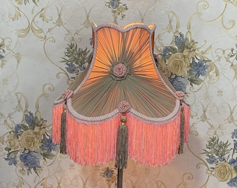 May include: A pink and green lampshade with a fringe trim and floral accents. The lampshade is made of fabric and has a pleated design.