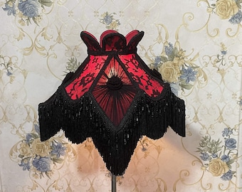 May include: A red and black lampshade with a fringe trim. The lampshade has a scalloped top and a geometric design.