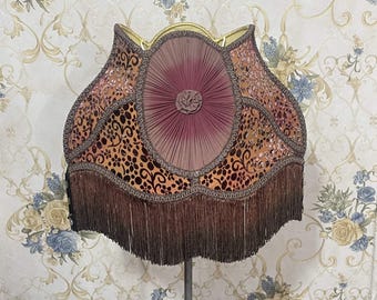 Op de afbeelding: Een bruine en gouden lampenkap met een franje rand en een bordeauxrode fluwelen middenpaneel. De lampenkap heeft een bloemenpatroon en is in vintage stijl.
