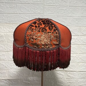 May include: A brown lampshade with a floral pattern and a fringe trim. The lampshade is made of fabric and has a round shape.