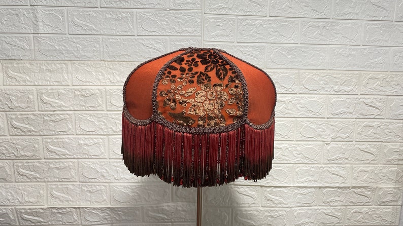 May include: A brown lampshade with a floral pattern and a fringe trim. The lampshade is made of fabric and has a round shape.