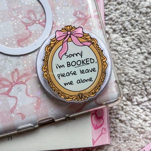 Puede incluir: Una pegatina con marco blanco y dorado con un lazo rosa y el texto "¡Lo siento! Estoy RESERVADO, por favor déjame en paz."