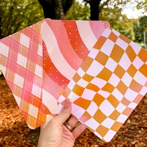 Può includere: Tre carte decorative con diversi motivi. La prima carta ha un motivo a quadri rosa e bianco. La seconda carta ha un motivo ondulato rosa e bianco con pois bianchi. La terza carta ha un motivo a quadri giallo e bianco.