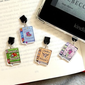 Peut inclure: Quatre marque-pages en forme de livre colorés avec des thèmes différents : hockey, football, cowboy et romance. Chaque marque-page est doté d’un clip noir sur le dessus et présente un fond blanc avec des illustrations colorées et le mot « Romance » imprimé sur le dos.