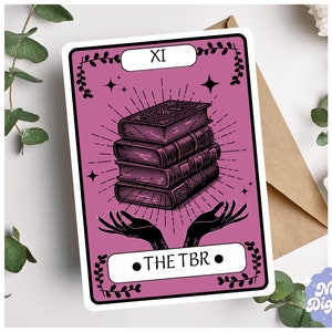 Può includere: Una carta dei tarocchi rosa con illustrazioni nere di una pila di libri, mani e accenti floreali. Il numero della carta "XI" e il testo "THE TBR" sono stampati sulla carta.