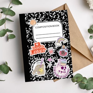 May include: Black and white composition book with various colorful stickers, including a book lover sticker, a coffee sticker, a skull sticker, and a rainbow sticker. The book has the text "COMPOSITION BOOK" printed on the front.