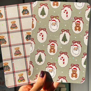 May include: Two Christmas-themed decorative paper sheets. One features a repeating pattern of teddy bears in plaid sweaters on a cream background with red grid lines. The other has a repeating pattern of Santa Claus, Christmas trees, candy canes, and teddy bears.