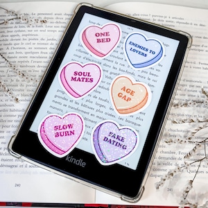 Może przedstawiać: Sześć naklejek w kształcie serca z brokatem i tekstem. Naklejki mówią "One Bed", "Soul Mates", "Enemies to Lovers", "Age Gap", "Slow Burn" i "Fake Dating".