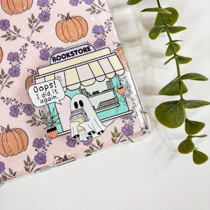 May include: A clear phone case with a pink floral and pumpkin pattern. A bookstore-themed pin features a ghost holding books with the text "Oops! I did it again."