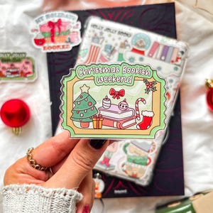 Könnte beinhalten: Ein klarer Aufkleber mit einem grünen und gelben Rand mit einem Weihnachtsbaum, Büchern und einer Zuckerstange. Der Text "Christmas Bookish weekend" wird angezeigt. Weitere Aufkleber und Weihnachtsschmuck sind ebenfalls sichtbar.