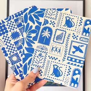 Peut inclure: Trois cartes carrées avec des motifs bleus et crème sont présentées. Les motifs comprennent des motifs tropicaux comme des palmiers, des singes et des formes géométriques. Les cartes sont devant un cadre.