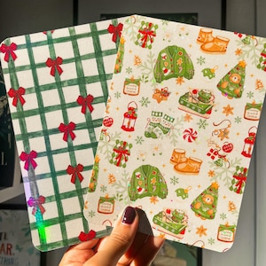 Puede incluir: Dos tarjetas decorativas con temática navideña. Una tarjeta presenta un patrón de cuadros verdes y blancos con lazos rojos. La otra tarjeta tiene un diseño festivo con suéteres navideños, botas y un árbol de Navidad con un oso.
