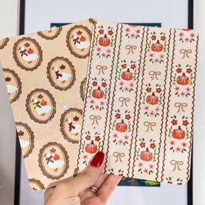 Può includere: Due biglietti decorativi con motivi autunnali. Uno presenta oche in cornici ovali con foglie. L'altro ha zucche, fiocchi e fiori. Entrambi i biglietti hanno uno sfondo beige.