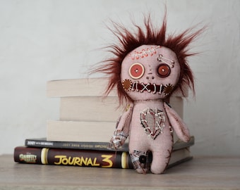 May include: A handmade rag doll with a stitched-on heart, red button eyes, and a messy brown hairdo. The doll is sitting on a stack of books with the title "JOURNAL 3" visible.