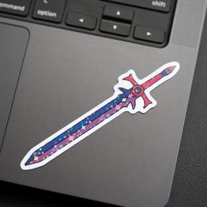 May include: A sticker of a sword with a red hilt and a blue and purple blade, decorated with stars. The sticker is on a laptop. The sword design has a white outline.