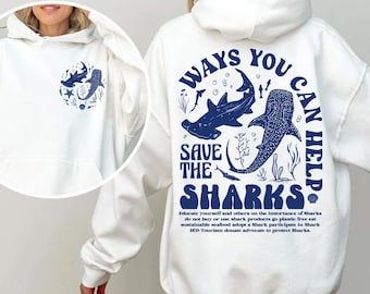May include: White hooded sweatshirt with a front pocket. The back displays a blue graphic with the text "WAYS YOU CAN HELP SAVE THE SHARKS" and shark illustrations. A smaller shark design is on the front.
