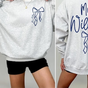 May include: Gray sweatshirt with a blue bow and the text "Mrs. William" on the back.