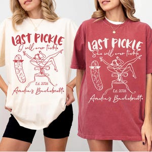 May include: Ivory and crimson t-shirts with a graphic design. The design includes the text "LAST PICKLE" and "I will ever tickle" or "She will ever tickle", along with a pickle illustration and the text "Est. 2026 Amelia's Bachelorette."